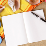 Blank journal with writing pen sitting on a brightly colored beach blanket with a pair of blue flip-flop sandals.