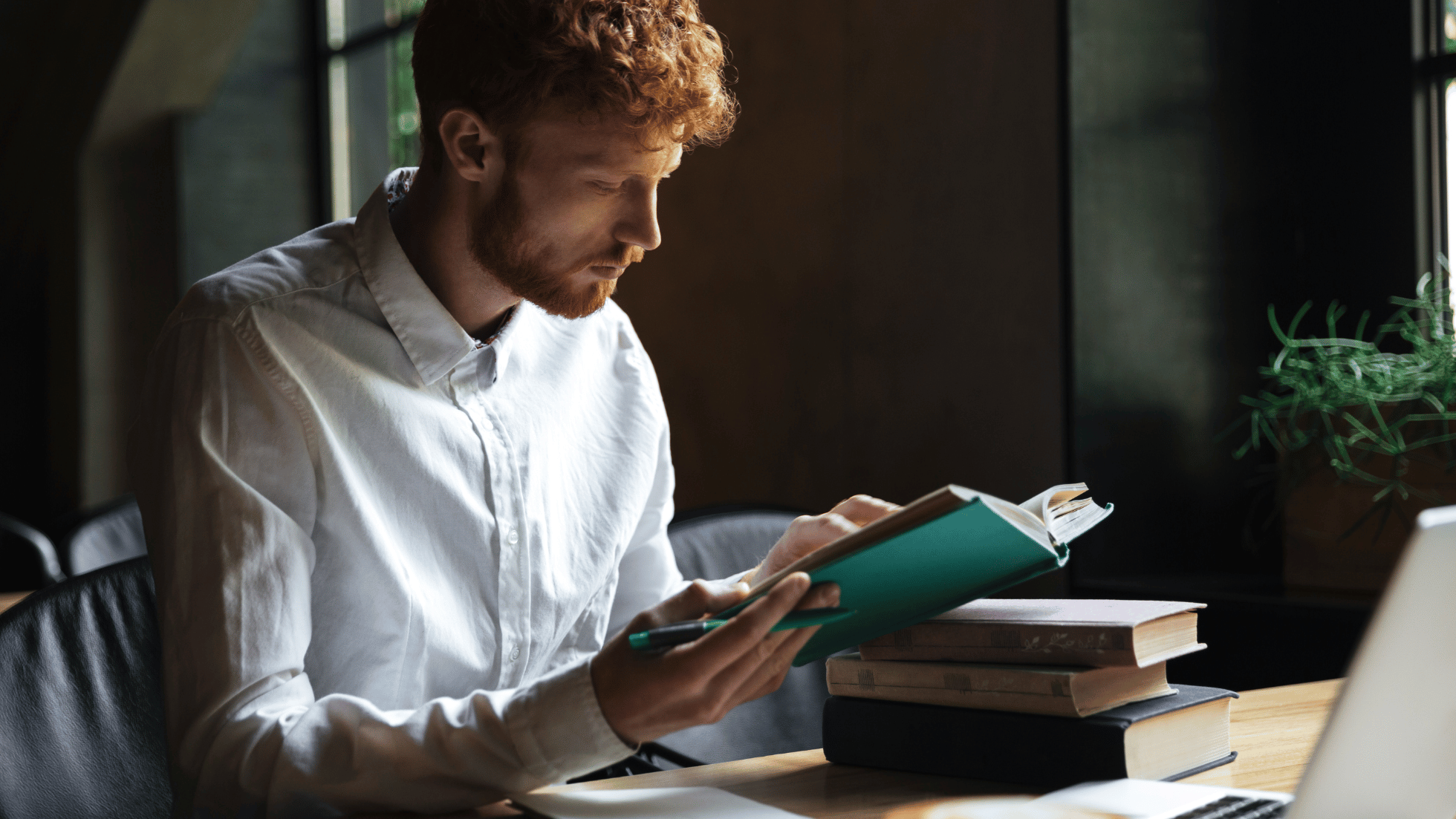 Young man with curly hair and short beard wearing a white button-up shirt holds a small notebook with advice from his dear mother. These make great high school graduate gifts.
